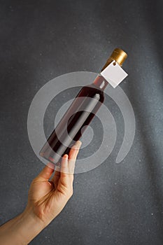 Male hand holding bottle of red wine, natural fruit alcohol liquor with empty label on grey background. Mock up, template for