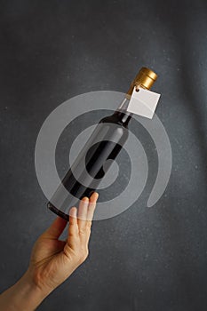 Male hand holding bottle of red wine, natural fruit alcohol liquor with empty label on grey background. Mock up, template for