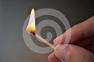 Male hand holding burning safety match stick with a flame getting close to the hand