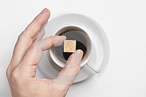 Male hand holding cane sugar cube over cup of black coffee against white background top view with space for text