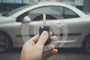 Male hand holding car keys with car on background. Man uses remote vehicle key to lock the car. Driver has parked the