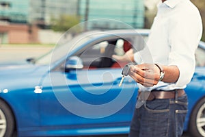 Male hand holding car keys offering new car on background