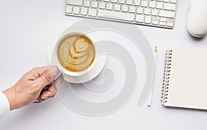 Male hand holding coffee cup latte art on white modern working table