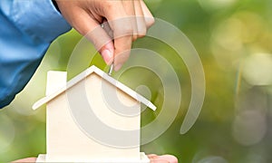 Male hand holding coins and piggy house bank save money, green nature background. Investment and save Concept.