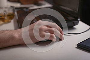 Male hand holding computer mouse with laptop keyboard in the background