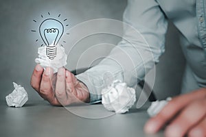 Male hand holding crumpled white paper and illuminated light bulb icons for finding great inspiration