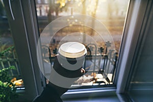 Male hand holding cup of coffee morning sun against the window