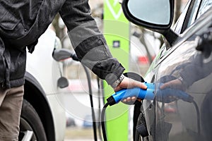 Male hand holding electrical socket while charging electrocar