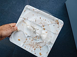 Male Hand Holding Empty Plastic Cake Tray with Traces and Crumbs on Blue