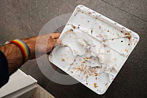 Male Hand Holding Empty Plastic Cake Tray with Traces and Crumbs on Stone
