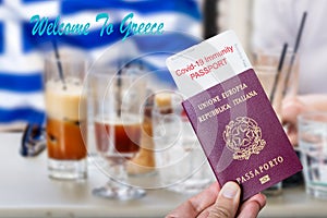 Male hand holding an european passport with a covid-19 immunity certificate over the Greek flag cold coffee background.