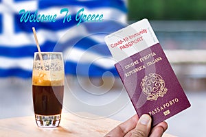 Male hand holding an european passport with a covid-19 immunity certificate over the Greek flag and a frape coffee. photo