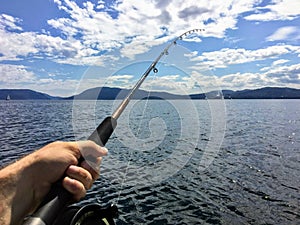 A male hand holding a fishing rod jigging for fish with the beautiful coastline of British Columbia Canada in the background. photo
