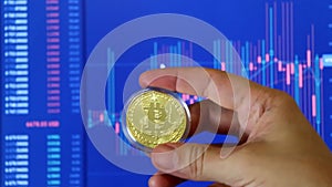 Male hand holding gold bitcoin coin and moves on BTC/USD chart background