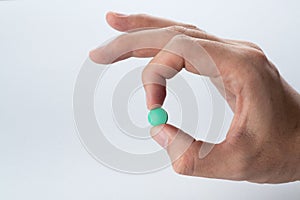 Male hand holding a green pill on a grey background.