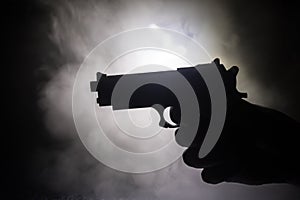 Male hand holding gun on black background with smoke toned back lights