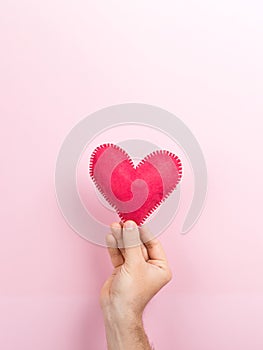 Male hand holding a handmade heart on a pink background. Valentine`s day concept, symbol of love, print commercial blank, copy
