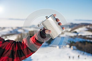 Male hand holding hip flask on a snowy mountain