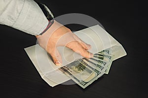 Male hand holding its fingers on white envelope full of American Dollars