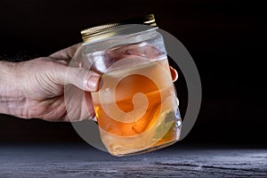 Male hand holding a jar that contains kombucha tea and kombucha scoby (also called as mother).