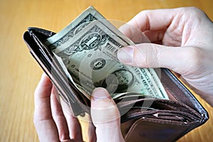 Male hand holding a leather wallet and withdrawing American currency (USD, US Dollars)