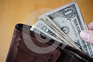 Male hand holding a leather wallet and withdrawing American currency (USD, US Dollars)