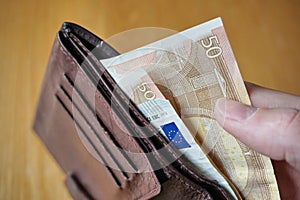 Male hand holding a leather wallet and withdrawing European currency (Euro, EUR)