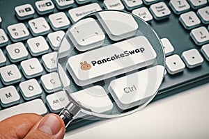 Male hand holding magnifying glass and focusing computer key with pancakeswap altcoin logo photo