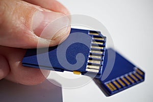 Male hand holding a memory card (SD card - Secure Digital card) used in video cameras and computers in blue color