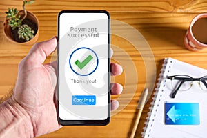 Male hand holding mobile phone with payment app interface showing payment successful message with green check mark. Credit card in