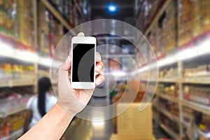 Male hand holding mobile smart phone on Supermarket blur background, business concept