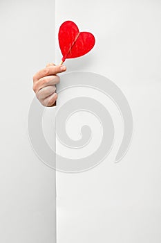 Male hand holding and offering Heart Lollipop behind white wall background