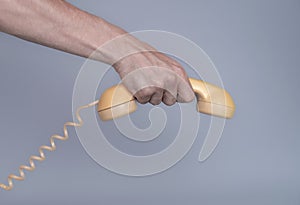 Male hand holding an old yellow plastic telephone receiver on gray background. Close up remote handset from a retro