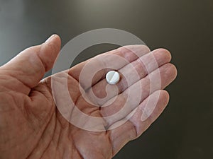 Male hand holding one pill in hand on grey background