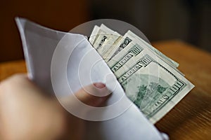 Male hand holding and passing a white envelope full of American Dollars (USD, US Dollars) as a symbol of illegal cash transfer, mo