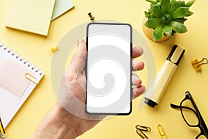 Male hand holding a phone with white screen over an office desk