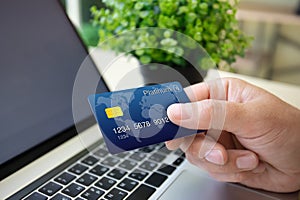 male hand holding plastic credit card background laptop in office