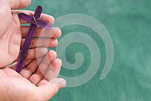 Male hand holding purple wooden cross flat lay in green background. Holy week and lent season concept