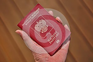 Male hand holding a Russian passport with captions Passport and Russian Federation in Cyrillic alphabet