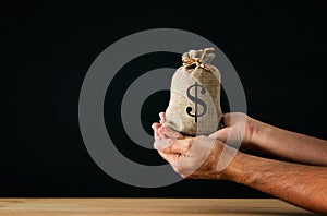 Male hand holding a sack of money over wooden desk
