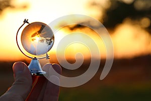 male hand holding small crystal globe in front of sunset