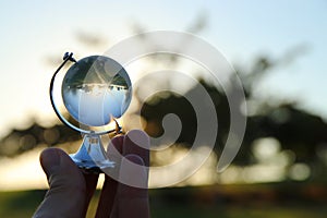 male hand holding small crystal globe in front of sunset