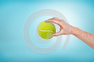 Male hand holding small tennis ball between fingers on blue background