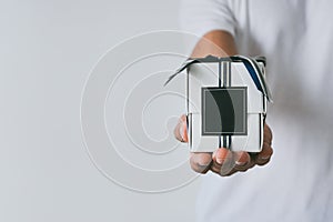Male hand holding a small white gift box wrapped with blue and silver color ribbon and dark blue blank label on white background