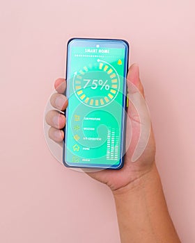 Male hand holding smart phone on pink background with smart home technology interface on smartphone app screen. Concept of