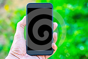 Male hand holding a smartphone on a tree bokeh background using a wallpaper or background for communication work.