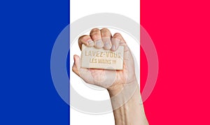 Male hand holding soap with words: Lavez-vous les mains, French flag background