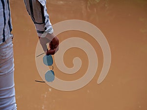 Male hand holding sunglasses at soiled water blur