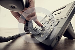 Male hand holding telephone receiver and dialing a phone number