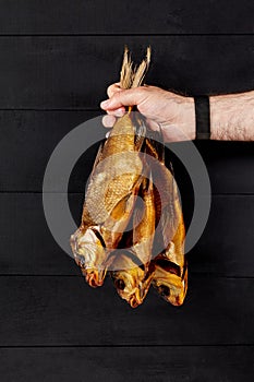 Male hand holding three smoked breams on black wooden background